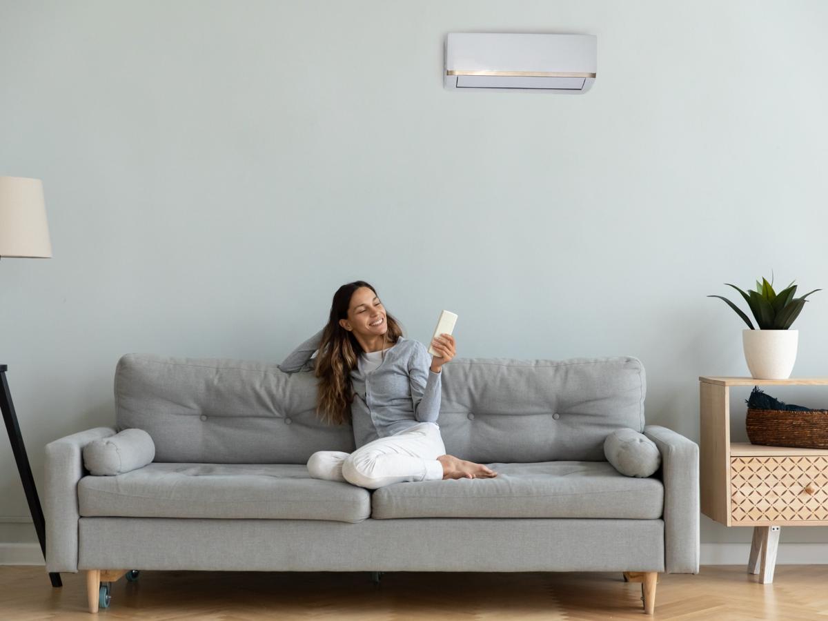 Woman relaxing on sofa with remote, using air conditioner