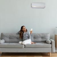 Woman relaxing on sofa with remote, using air conditioner