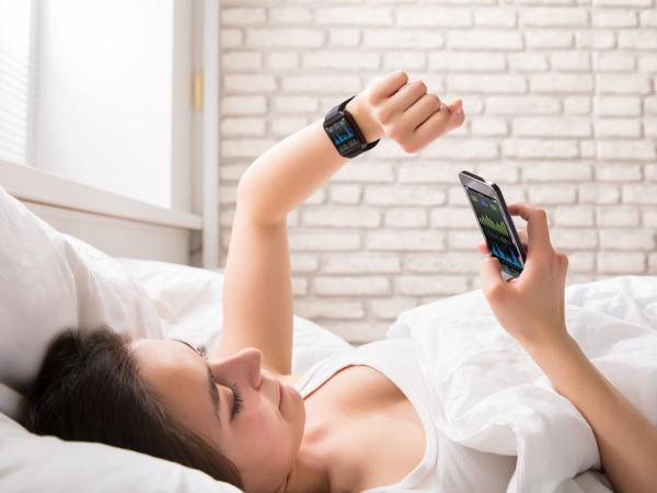 Woman synchronizing smartwatch with phone in bed